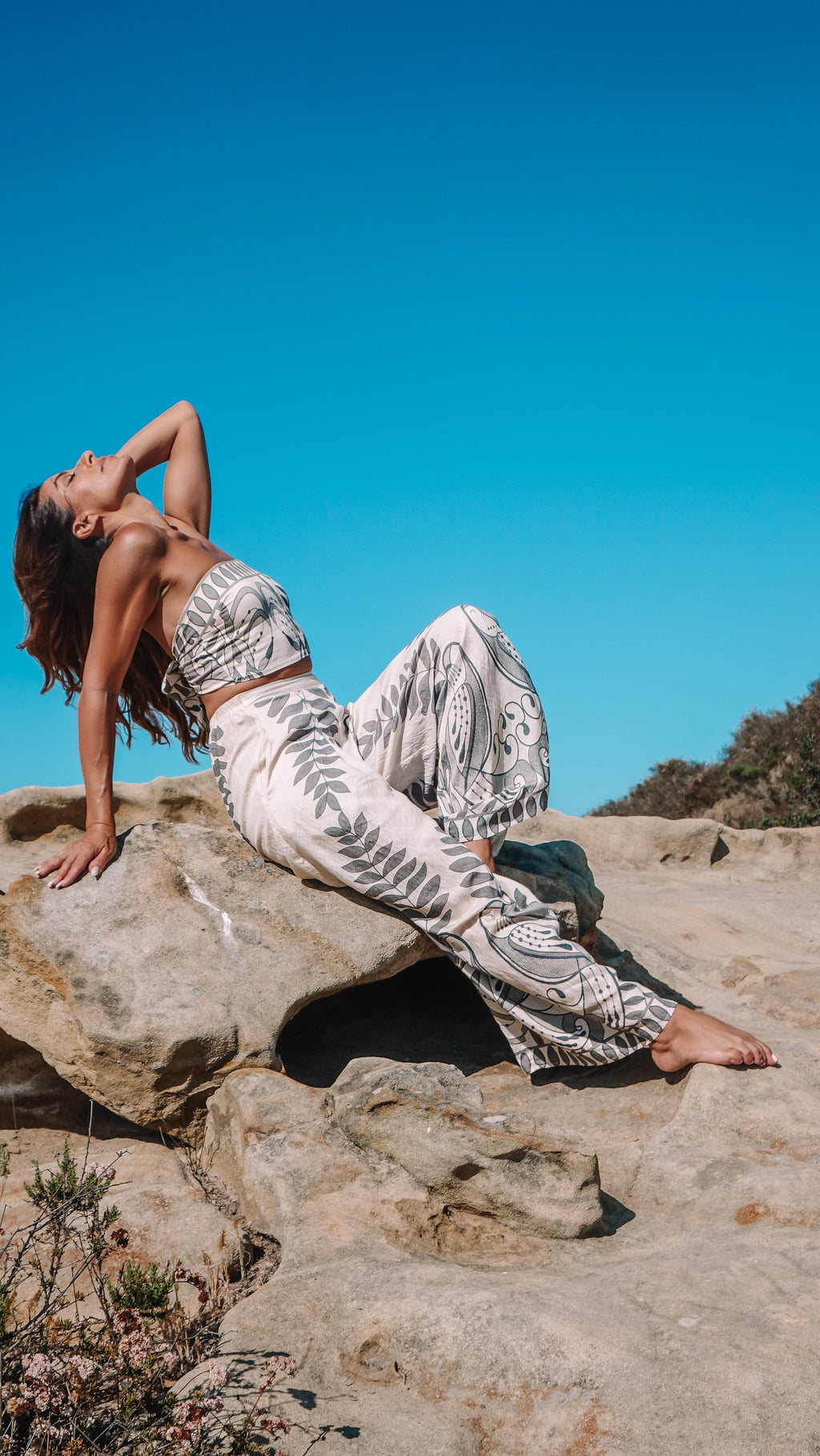 Model wearing the Kinnaree Paros Set on a rocky coastline beneath a clear blue sky